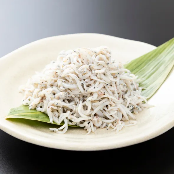 white plate with a heap of small whitebait fish on a green leaf
