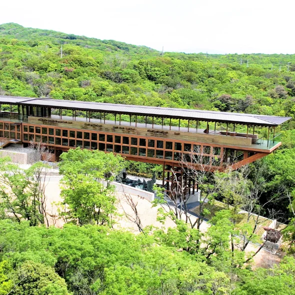 An elevated view of the wooden Zenbo Seinei wellness facility surrounded by lush green trees and rolling hills on Awaji Island.