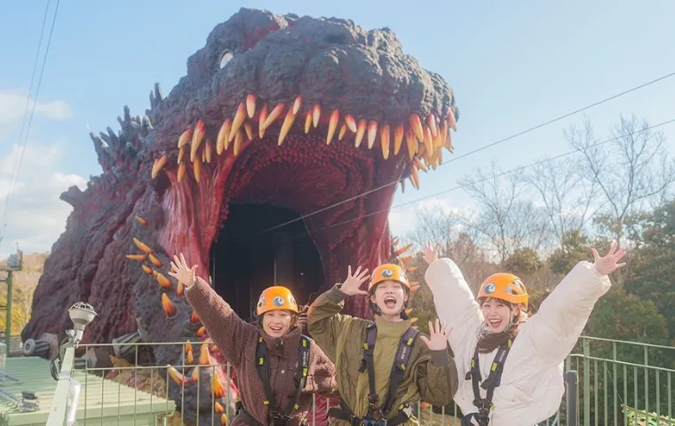 Excited visitors in zipline gear prepear to fly toward life size Godzilla at Nijigen no Mori Awaji Island