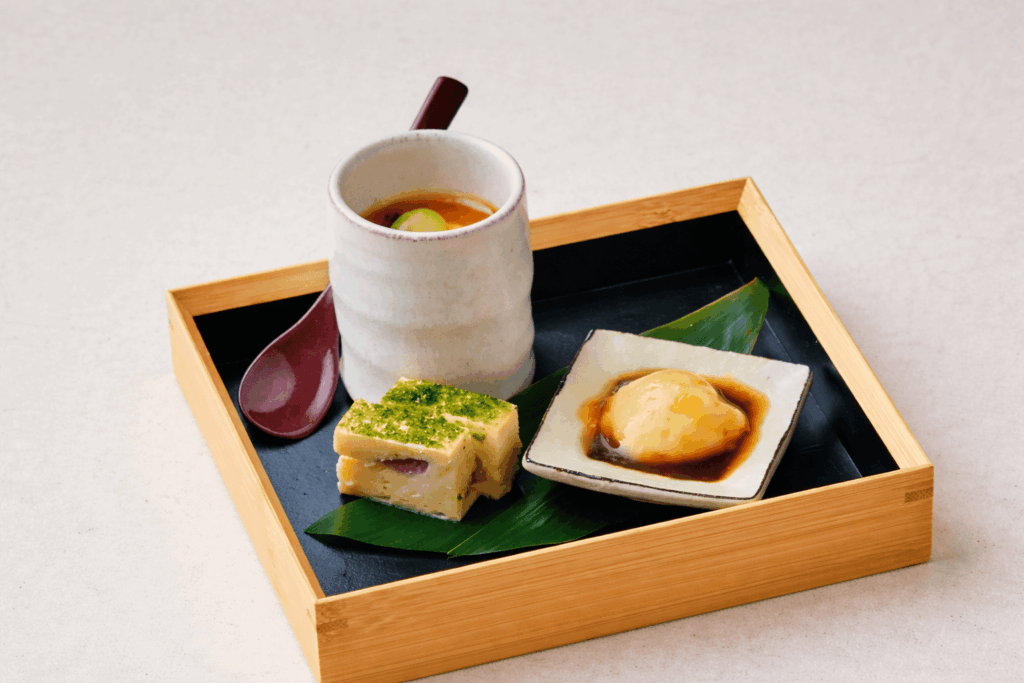 Traditional Japanese appetizer set with chawanmushi, tofu, and seasonal delicacies served in a bamboo tray