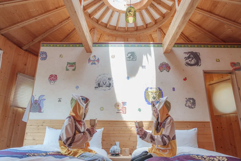 Guests in Monster Hunter themed pajamas sitting on beds in cocoon villa bedroom with game-inspired wallpaper at Grand Chariot Awaji Island
