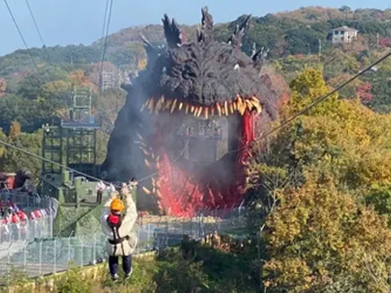 Visitor riding the Godzilla zipline toward the giant Godzilla statue at Nijigen no Mori on Awaji Island, Japan